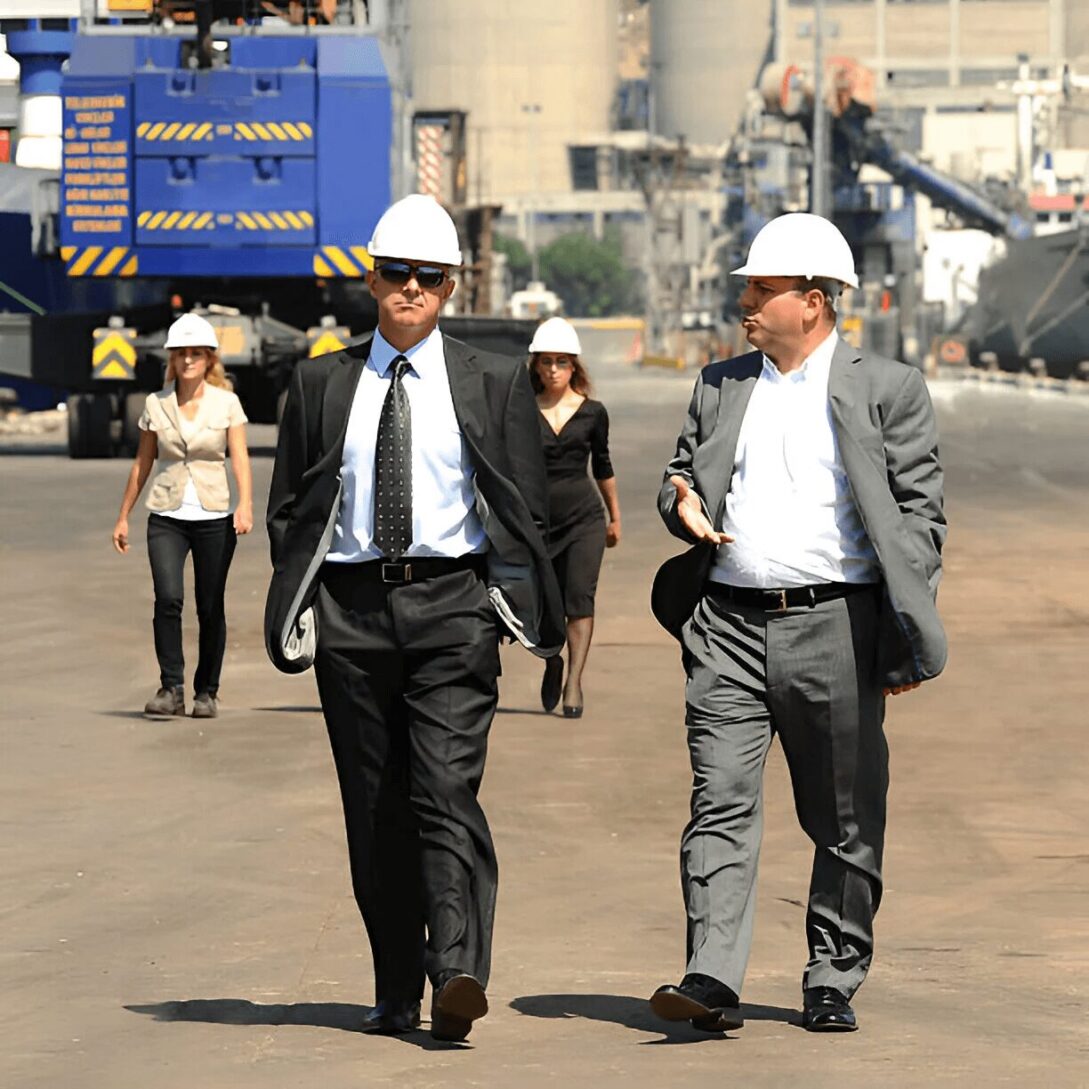 Two men in suits and hard hats walk down a street.